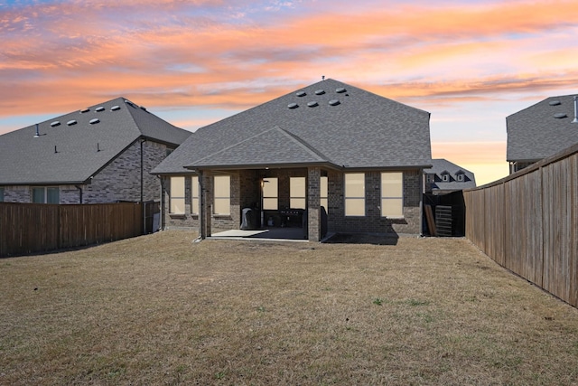 back of house featuring a yard, a fenced backyard, a shingled roof, and brick siding