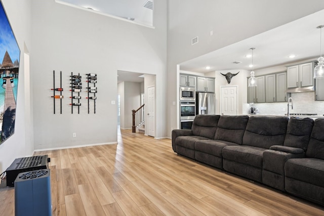 living room featuring light wood-type flooring, visible vents, stairway, and baseboards