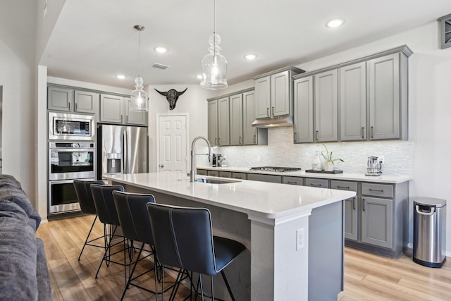 9017 Cattle Herd Dr, Fort Worth, TX 76123 - kitchen featuring gray cabinetry, a sink, appliances with stainless steel finishes, a kitchen bar, and light wood finished floors