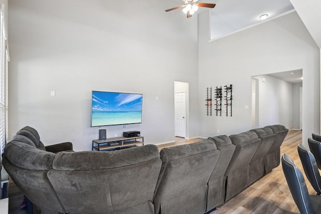 living room with ceiling fan, a high ceiling, and wood finished floors