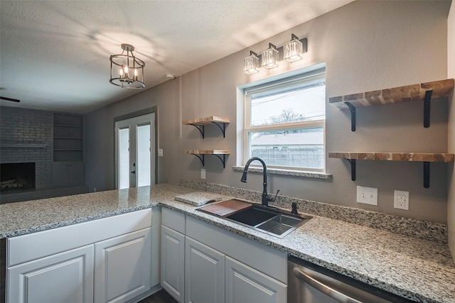 kitchen with open shelves, stainless steel dishwasher, a brick fireplace, a sink, and a peninsula