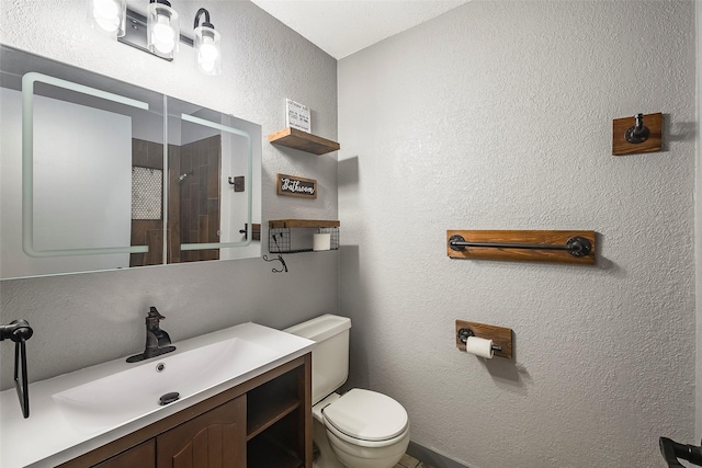 full bathroom featuring a textured wall, tiled shower, vanity, and toilet