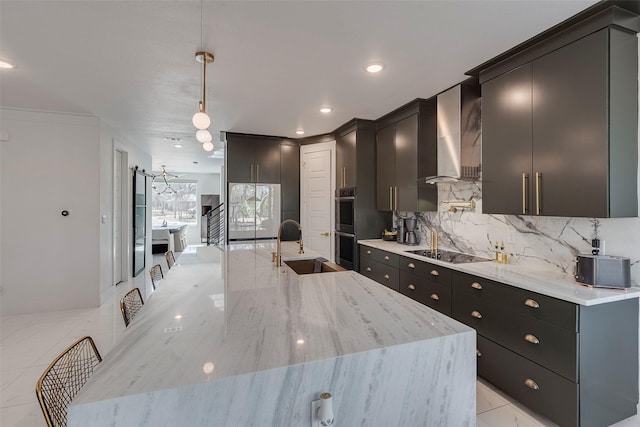 kitchen with black electric cooktop, dark cabinets, hanging light fixtures, wall chimney range hood, and tasteful backsplash