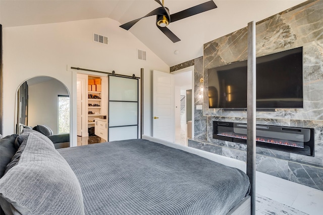 bedroom with a glass covered fireplace, visible vents, ceiling fan, and a barn door