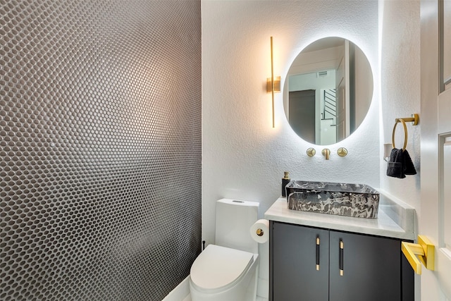 bathroom featuring a textured wall, vanity, and toilet