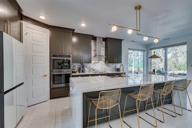 kitchen featuring marble finish floor, double oven, freestanding refrigerator, a sink, and wall chimney exhaust hood