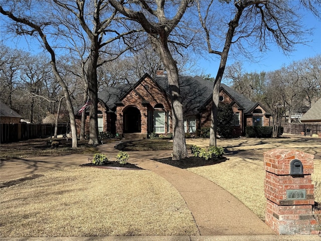 view of front facade with brick siding, a chimney, and fence