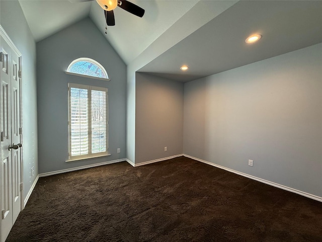 spare room with a ceiling fan, vaulted ceiling, dark carpet, and baseboards