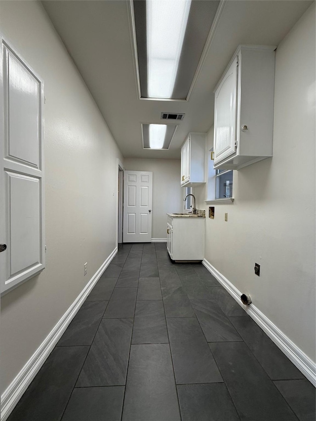 laundry area featuring cabinet space, baseboards, visible vents, dark tile patterned flooring, and a sink