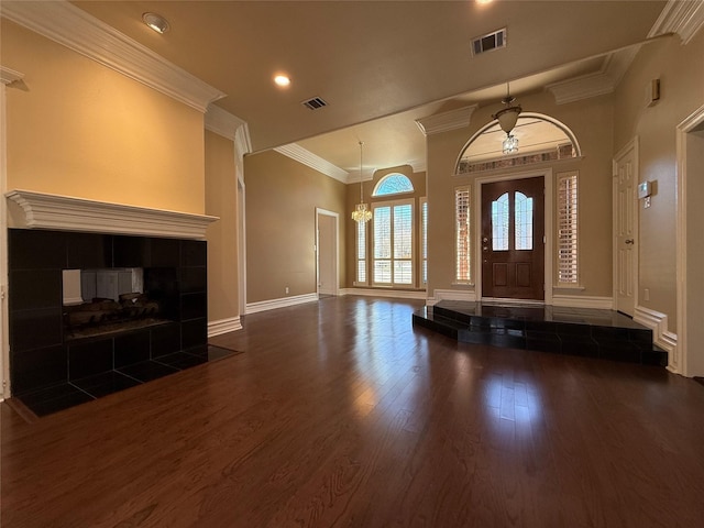 entryway with baseboards, visible vents, a tiled fireplace, ornamental molding, and wood finished floors