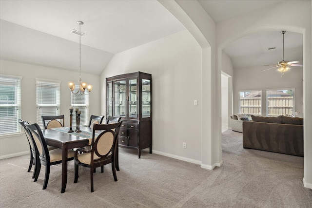 dining room with arched walkways, light colored carpet, ceiling fan with notable chandelier, baseboards, and vaulted ceiling