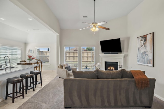 living area featuring light tile patterned floors, visible vents, ceiling fan, a lit fireplace, and baseboards