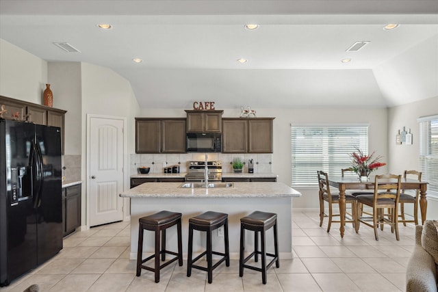 kitchen featuring an island with sink, black appliances, vaulted ceiling, and a sink