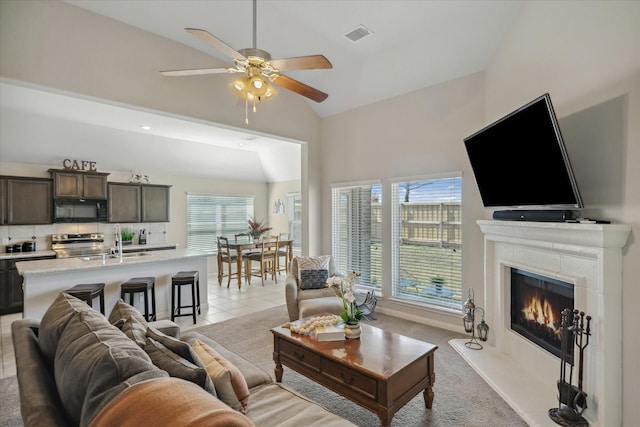 living area featuring visible vents, a ceiling fan, light carpet, light tile patterned flooring, and a lit fireplace