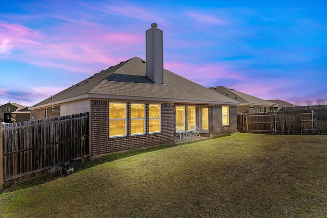 rear view of property featuring a yard, a fenced backyard, a chimney, and brick siding