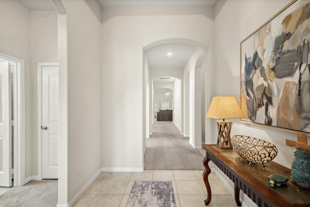 hallway with arched walkways, light tile patterned floors, light carpet, and baseboards