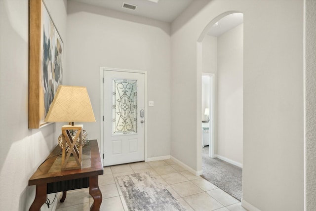 entryway featuring arched walkways, light tile patterned flooring, a towering ceiling, visible vents, and baseboards