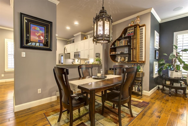 dining area featuring an inviting chandelier, wood-type flooring, baseboards, and ornamental molding