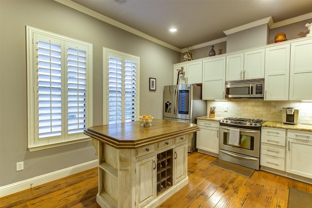 kitchen with crown molding, appliances with stainless steel finishes, light wood finished floors, and tasteful backsplash