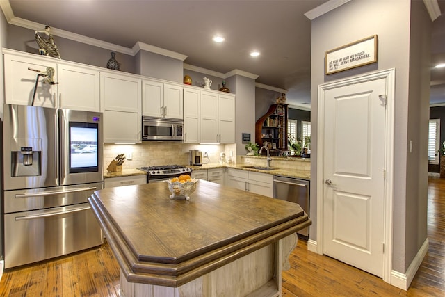 kitchen with stainless steel appliances, a sink, ornamental molding, tasteful backsplash, and wood-type flooring