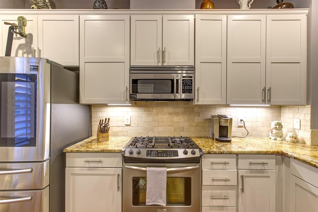 kitchen with white cabinets, light stone countertops, appliances with stainless steel finishes, and decorative backsplash