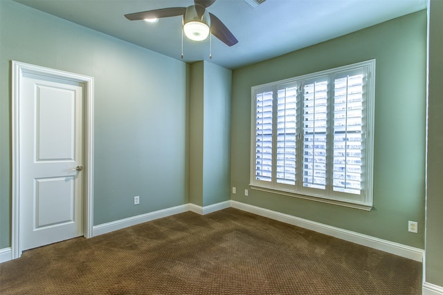 empty room with dark colored carpet, a ceiling fan, and baseboards