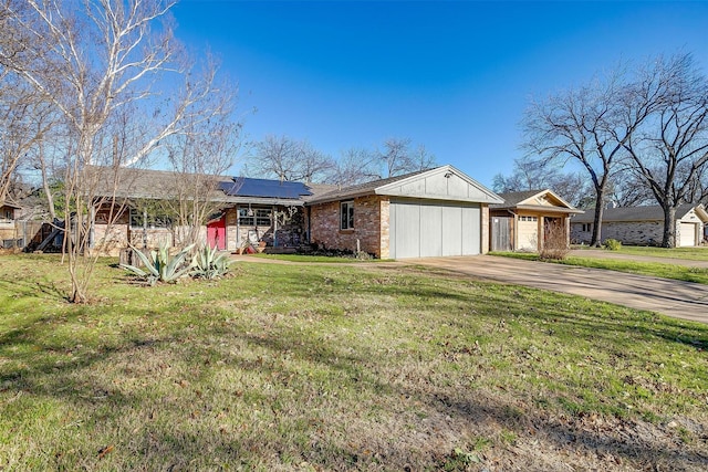 view of front facade with brick siding, solar panels, concrete driveway, an attached garage, and a front yard