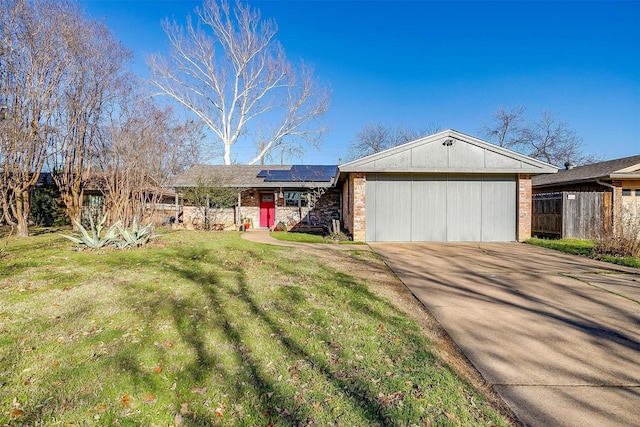 single story home with concrete driveway, an attached garage, fence, roof mounted solar panels, and a front lawn