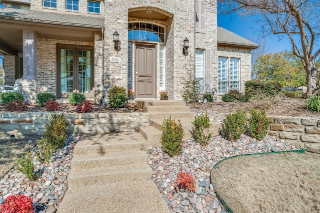 doorway to property with a shingled roof and brick siding