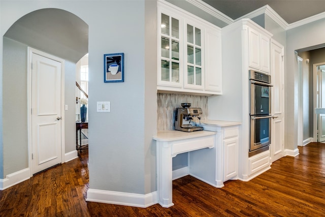 kitchen with arched walkways, double oven, white cabinetry, dark wood-style floors, and glass insert cabinets