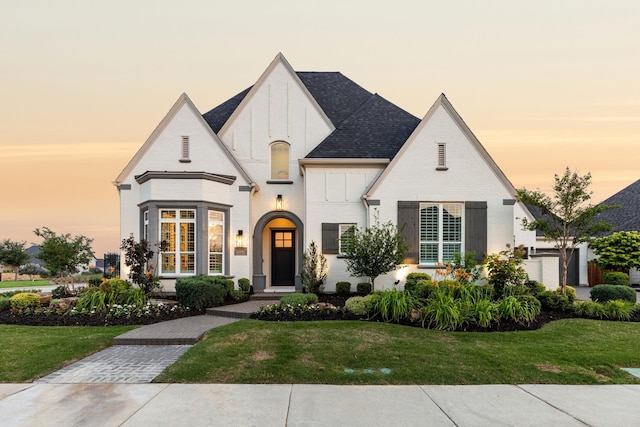 view of front of home featuring a shingled roof, a lawn, and brick siding