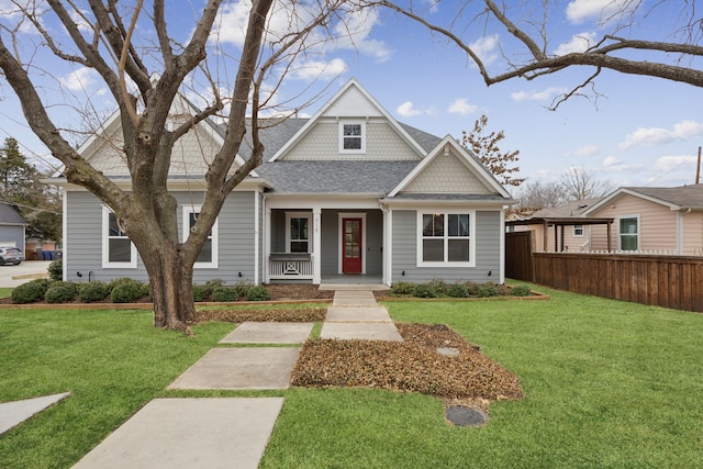 view of front of home featuring covered porch, a front lawn, roof with shingles, and fence