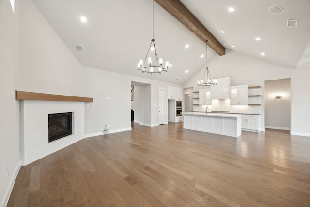 unfurnished living room featuring light wood finished floors, visible vents, a glass covered fireplace, high vaulted ceiling, and beamed ceiling