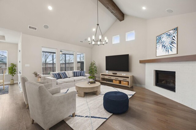 living area with visible vents, a brick fireplace, wood finished floors, a chandelier, and beamed ceiling