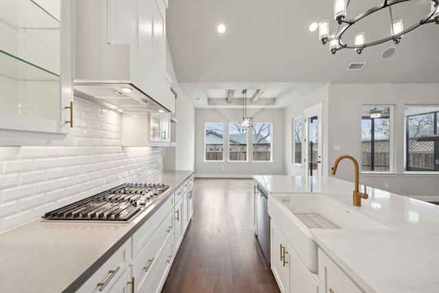 kitchen with stainless steel appliances, visible vents, white cabinetry, a sink, and premium range hood