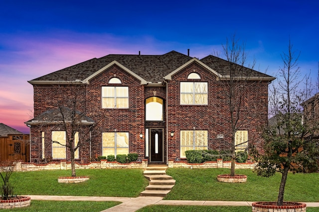 view of front of home with a shingled roof, a front yard, and brick siding