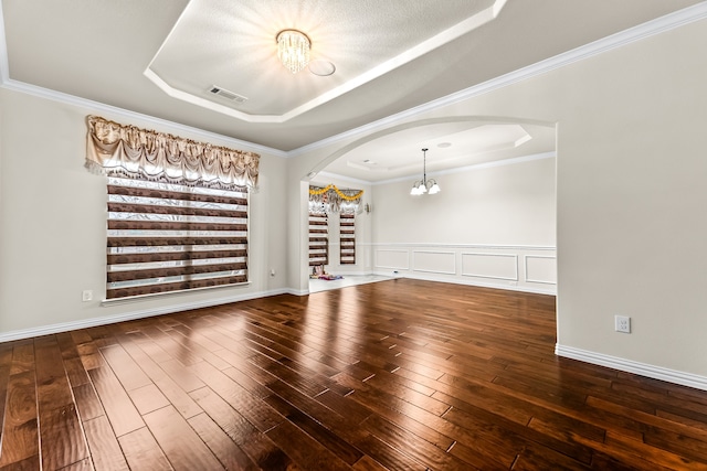 empty room featuring arched walkways, a tray ceiling, visible vents, wood finished floors, and a chandelier