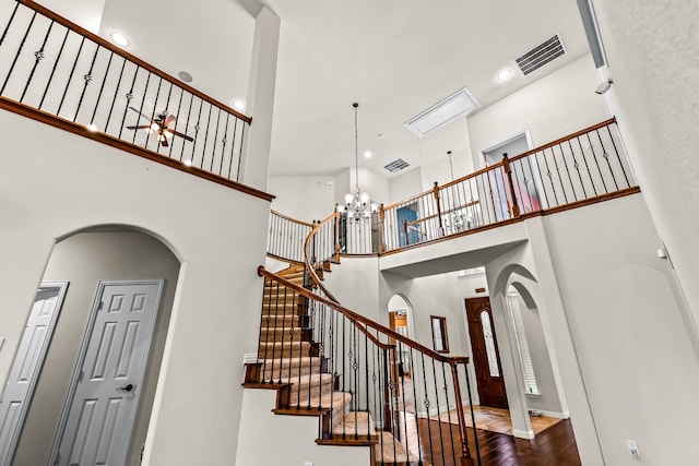 stairway featuring a towering ceiling, visible vents, arched walkways, and wood finished floors