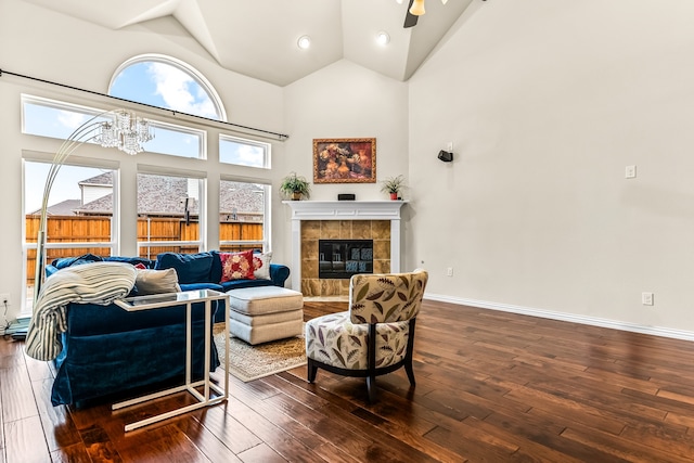 living area with baseboards, a tile fireplace, dark wood-style floors, an inviting chandelier, and high vaulted ceiling