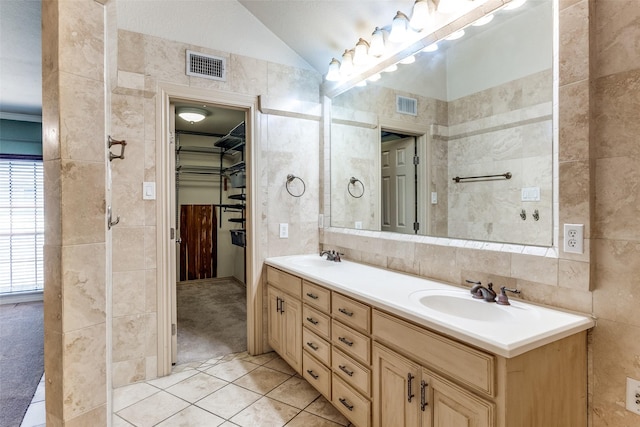 full bathroom featuring a sink, visible vents, vaulted ceiling, and tile walls