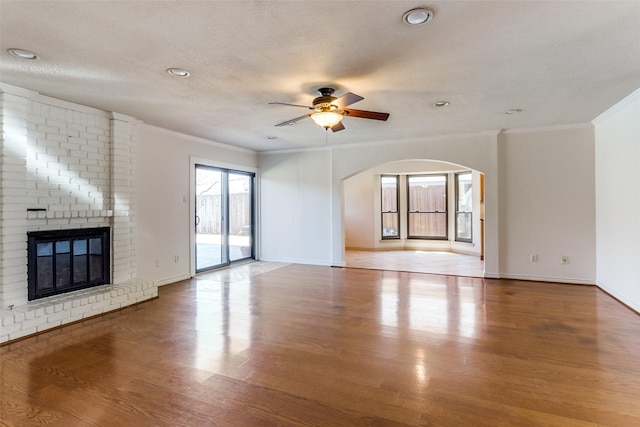 unfurnished living room featuring a fireplace, a ceiling fan, ornamental molding, a textured ceiling, and wood finished floors