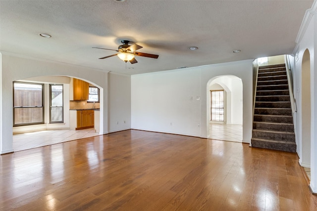 unfurnished living room with light wood finished floors, ornamental molding, and arched walkways