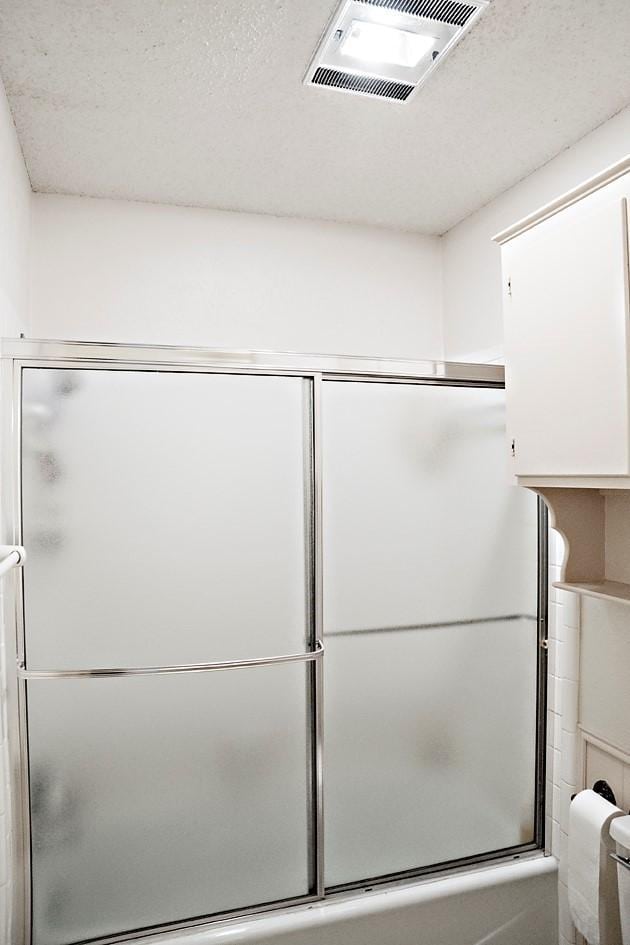 bathroom featuring toilet, combined bath / shower with glass door, and visible vents