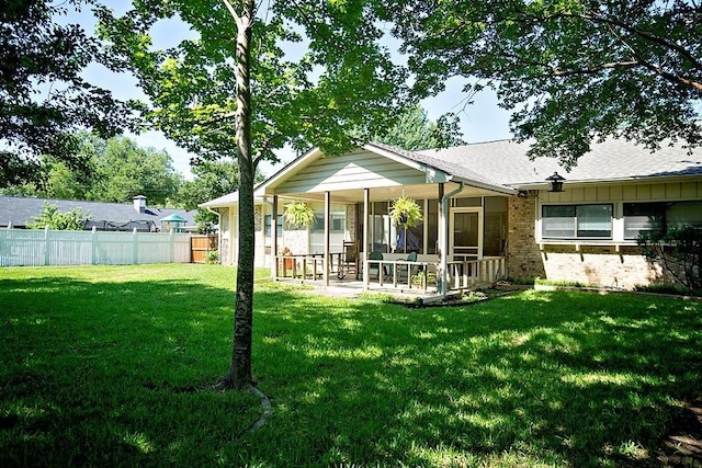 rear view of property with brick siding, fence, a sunroom, a yard, and board and batten siding