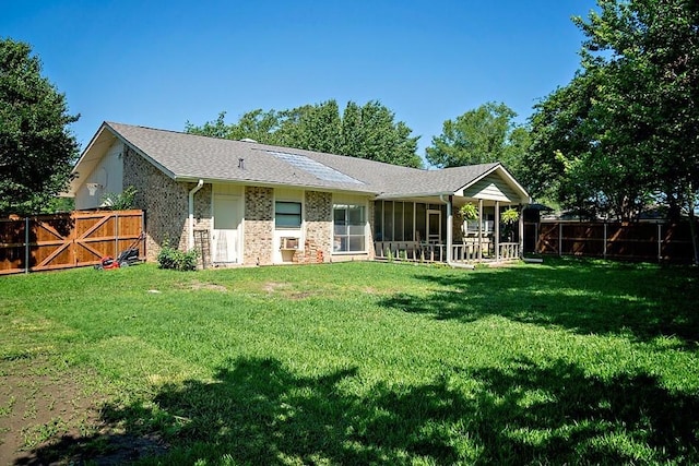 rear view of house with a fenced backyard, brick siding, a sunroom, a lawn, and a gate