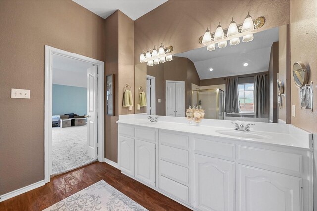 full bathroom with double vanity, a shower stall, a sink, and wood finished floors