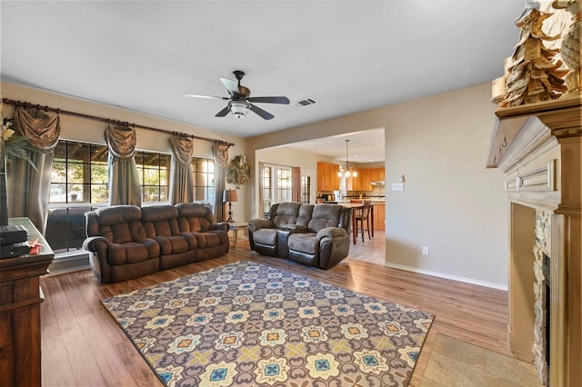 living room with ceiling fan with notable chandelier, baseboards, visible vents, and light wood-style floors