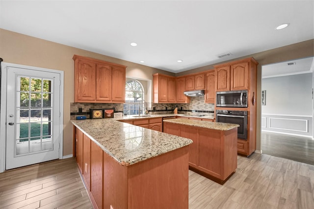 kitchen featuring a kitchen island, appliances with stainless steel finishes, light stone countertops, under cabinet range hood, and a sink