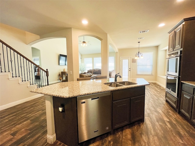 kitchen with stainless steel appliances, a sink, a center island with sink, and dark wood-style floors