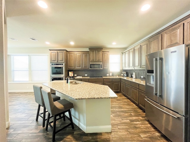 kitchen with stainless steel appliances, visible vents, decorative backsplash, a kitchen island with sink, and a sink